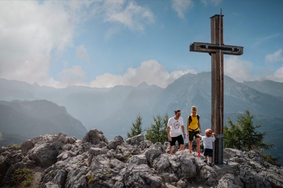 Wandern am Jenner Drei Wanderer stehen an einem Holzkreuz auf einem Berggipfel mit weitem Blick in die Ferne.
