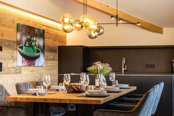 Die moderne Küche verfügt über einen Geschirrspüler, eine Kaffeemaschine und einen Backofen Moderne Küche mit Holztisch, eleganten Stühlen und stilvoller Beleuchtung.