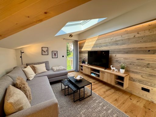 Über ein großzügiges Dachfenster erhält der Wohnbereich viel natürliches Licht Helles Wohnzimmer mit Couch, TV und Holzwänden unter einem Dachfenster.