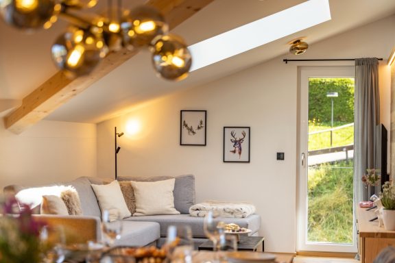 Der gemütliche Wohnbereich lädt zum Kuscheln ein Heller Wohnraum mit Sofa, Bildern an der Wand und Tür zu einem grünen Außenbereich.