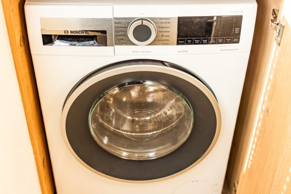 Eine hochwertige Waschmaschine von Bosch sorgt dafür, dass Ihre Reisewäsche frisch bleibt Moderne Waschmaschine mit transparentem Bullauge in minimalistischer Wohnungseinrichtung.