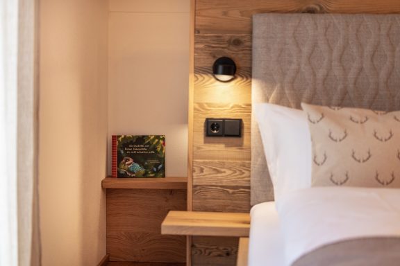 Hinter dem Kopfteil befindet sich ein gemütliches weiteres Bett für Groß oder Klein (90x200cm) Gemütliches Schlafzimmer mit Holzdetails, Nachttisch und Buch im Hintergrund.