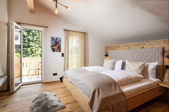 Das große Schlafzimmer „Hirsch“ bietet Platz für drei Erwachsene Helles Schlafzimmer mit Doppelbett, Fenster zur Terrasse und Holzfußboden.