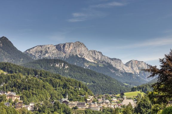 Balkonblick auf die historische Berchtesgadener Altstadt Berglandschaft mit hohen Gipfeln und einem grünen Tal und einem kleinen Dorf im Vordergrund.
