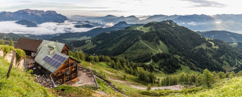 Purtschellerhaus Berglandschaft mit einer Hütte, umgeben von Wiesen und Bergen, im Morgengrauen.