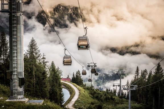 Die Jennerbahn Seilbahn über grünes Gelände mit Wolken und Bergen im Hintergrund.