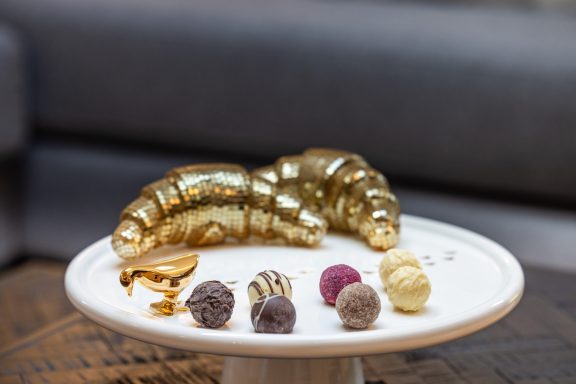 Ihr Alpenzuhause wurde mit viel Liebe zum Detail eingerichtet Goldene Croissants und bunte Pralinen auf einem weißen Teller.