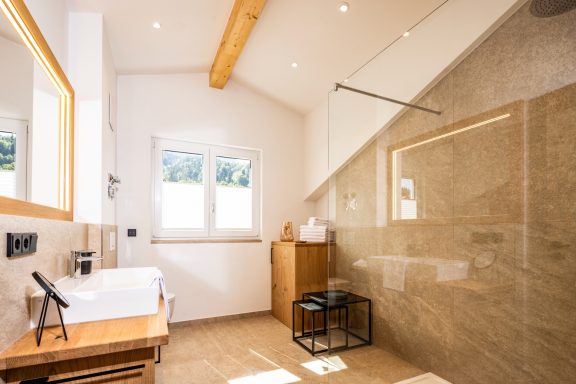 In der großen Walk-In Dusche lässt es sich erfrischt in den Tag starten Heller, moderner Badezimmers mit Holzdetails und großen Fenstern.